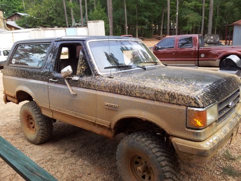 2012 Ford Bronco - This Ford Bronco is covered in mud after an off-road excursion, with a pickup truck visible in the background.