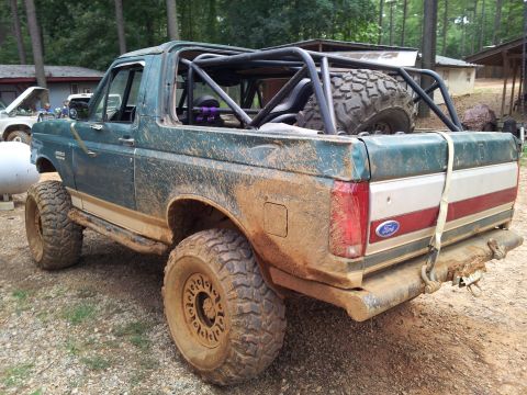 2012 Ford Bronco - This heavily modified Ford Bronco, covered in mud, features a custom roll cage and oversized tires, suggesting it's built for off-road use.