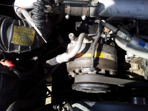 1994 GMC Sierra 3500 - A close-up view of engine components, including the air conditioning compressor and a warning label about turbocharger blades.