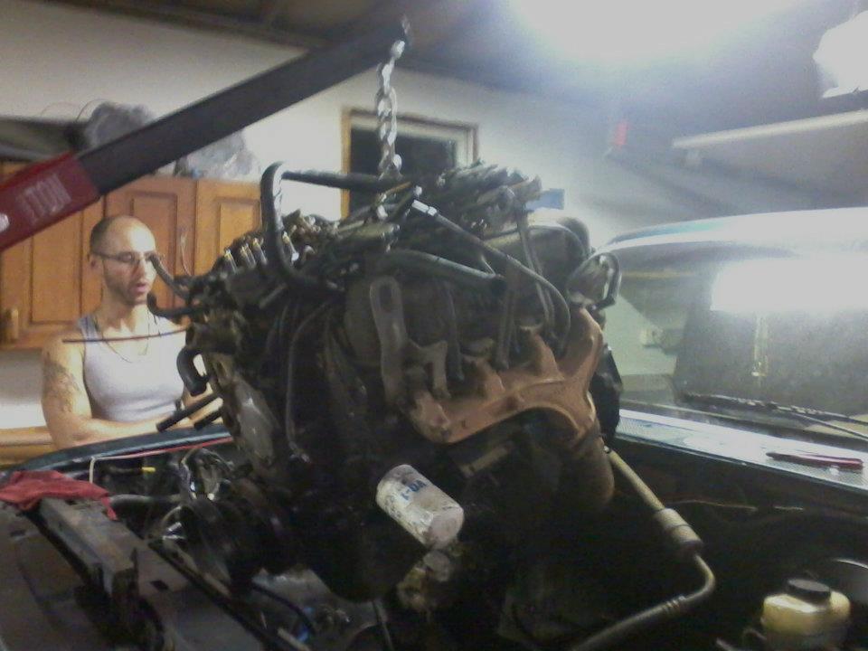 Man in garage with engine hoist lifting an engine out of a car