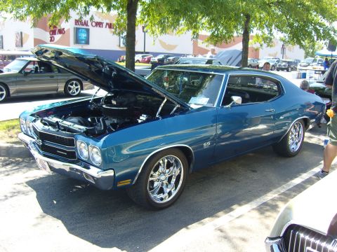 2007 Ford Mustang - A blue classic car is parked with its hood open, revealing the engine bay. Other vehicles and a building are in the background.