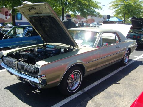 2007 Ford Mustang - A gold 1969 Mercury Cougar is displayed with its hood open at an outdoor car show.