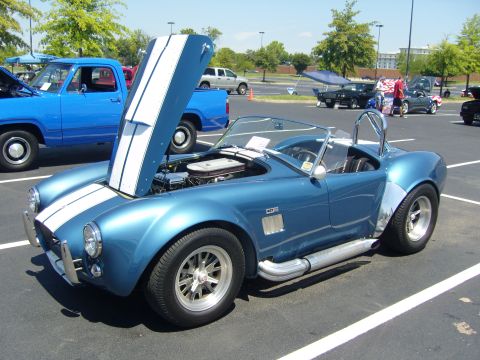 2007 Ford Mustang - Blue AC Cobra replica with racing stripes and side pipes at a car show.