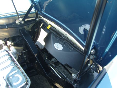 2007 Ford Mustang - The engine bay of a blue car is visible with the hood open, revealing the fan and various wires.