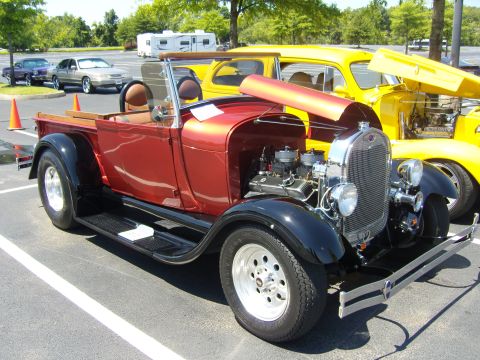 2007 Ford Mustang - A classic red pickup truck hot rod is parked in a lot, with its hood open, next to a yellow vehicle.