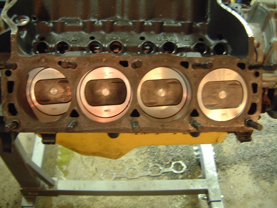 V8 engine block on a stand, four cylinders visible with pistons at the deck surface, head removed
