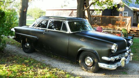 1954 Ford Crestline - A matte black 1954 Ford Crestline sedan sits parked outdoors, showing signs of wear and tear.