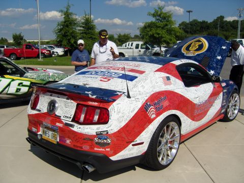 2007 Ford Mustang - 2007 Ford Mustang covered in signatures and American flag graphics, with another vehicle in the background.