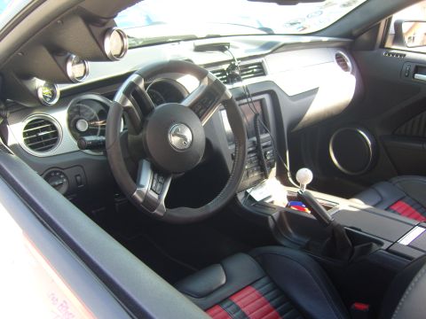 2007 Ford Mustang - The interior of a modified car features racing seats with red accents, a manual transmission shifter, and additional gauges mounted on the…