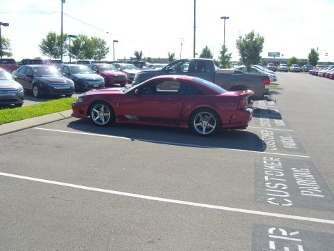 2007 Ford Mustang - A red 2007 Ford Mustang coupe is parked in a lot with other vehicles.