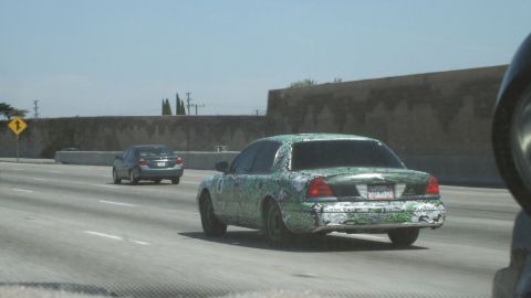 2003 Ford Crown Victoria - Rear three-quarter view of a sedan covered in green and black graffiti art wrap on the highway