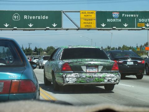 2003 Ford Crown Victoria - Rear view of an art-wrapped sedan in freeway traffic below green interchange signs