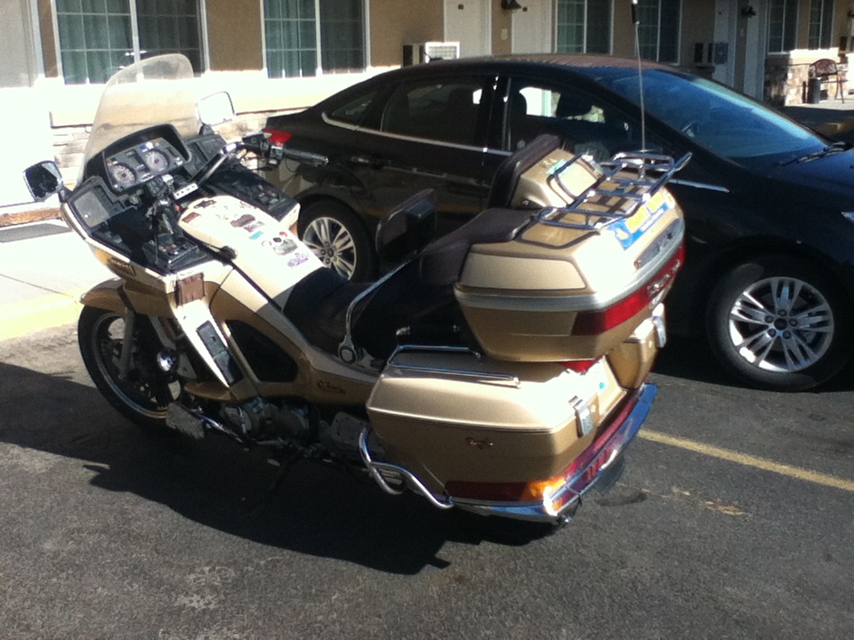 Gold touring motorcycle parked next to a dark sedan