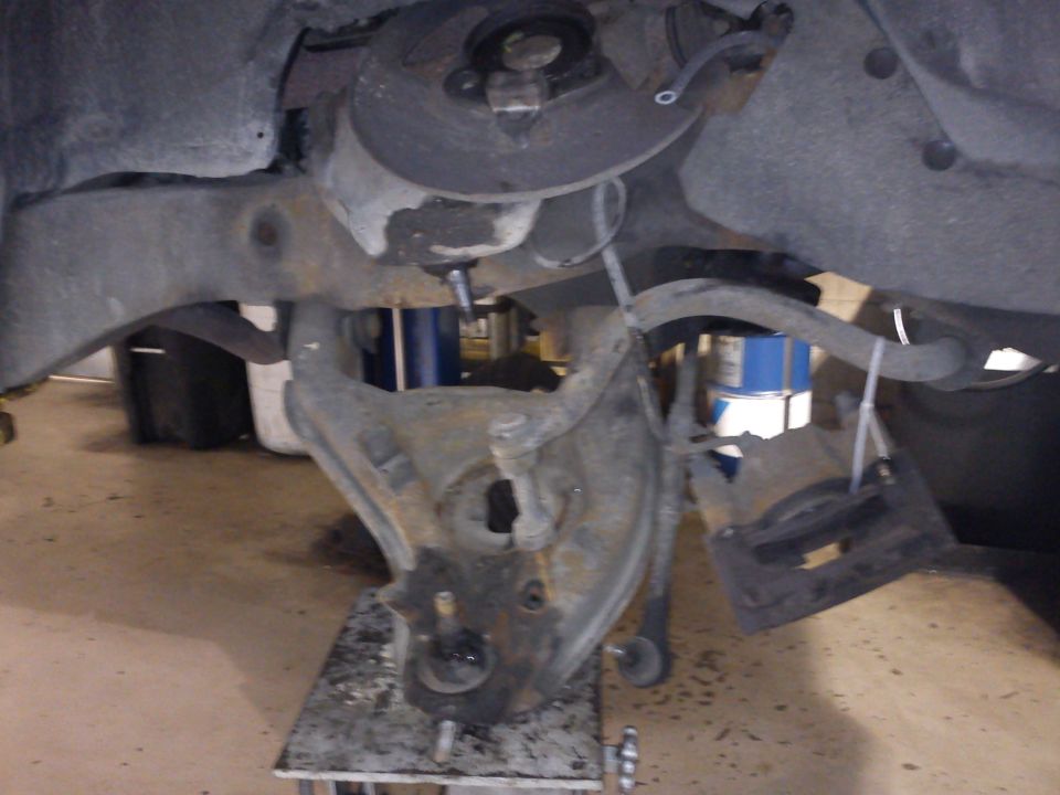 Front suspension disassembled on a truck, showing knuckle, control arm and ball joint supported by a stand in a garage