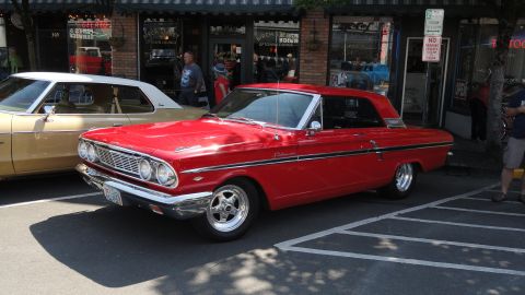 1964 Ford Fairlane - A red 1964 Ford Fairlane is parked on the street in front of a building with people walking by.