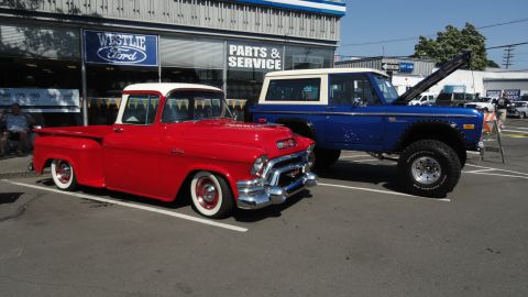 1964 Ford Fairlane - Two classic vehicles, a GMC pickup and a Ford Bronco, are parked outside a dealership.