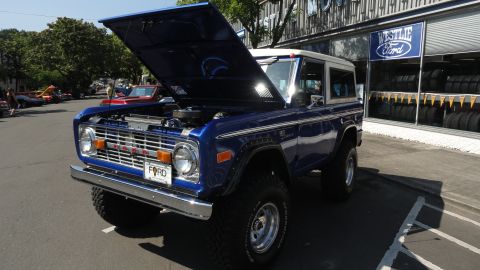 1964 Ford Fairlane - A blue Ford Bronco is parked outside a dealership with its hood up, showing the engine compartment.