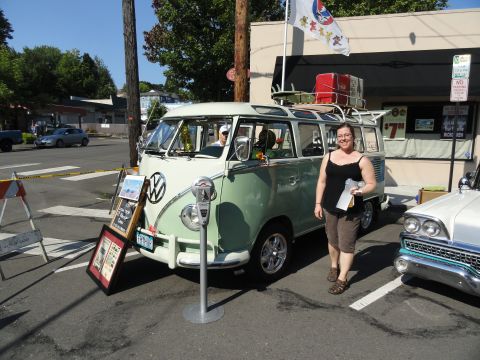 1964 Ford Fairlane - A woman stands next to a vintage Volkswagen Type 2 panel van, which is decorated with surfboards and luggage on its roof rack.