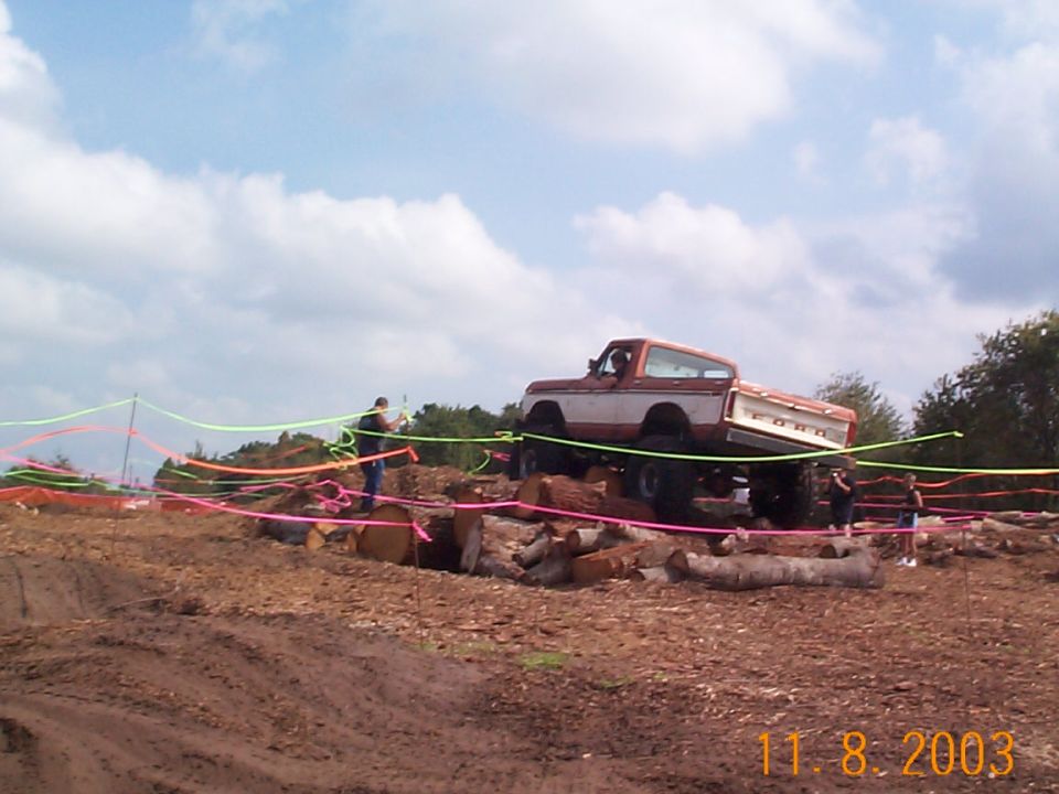 Red and white lifted Ford pickup climbing logs at an off-road obstacle course