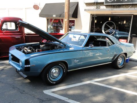 1964 Ford Fairlane - A blue 1969 Chevrolet Camaro SS is displayed with its hood open, parked beside a red pickup truck.