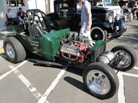 1964 Ford Fairlane - A custom green hot rod with a powerful engine is parked next to a classic black car at an outdoor event.