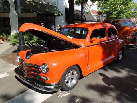 1964 Ford Fairlane - An orange sedan with its hood open is parked on a street, with a vintage truck behind it.