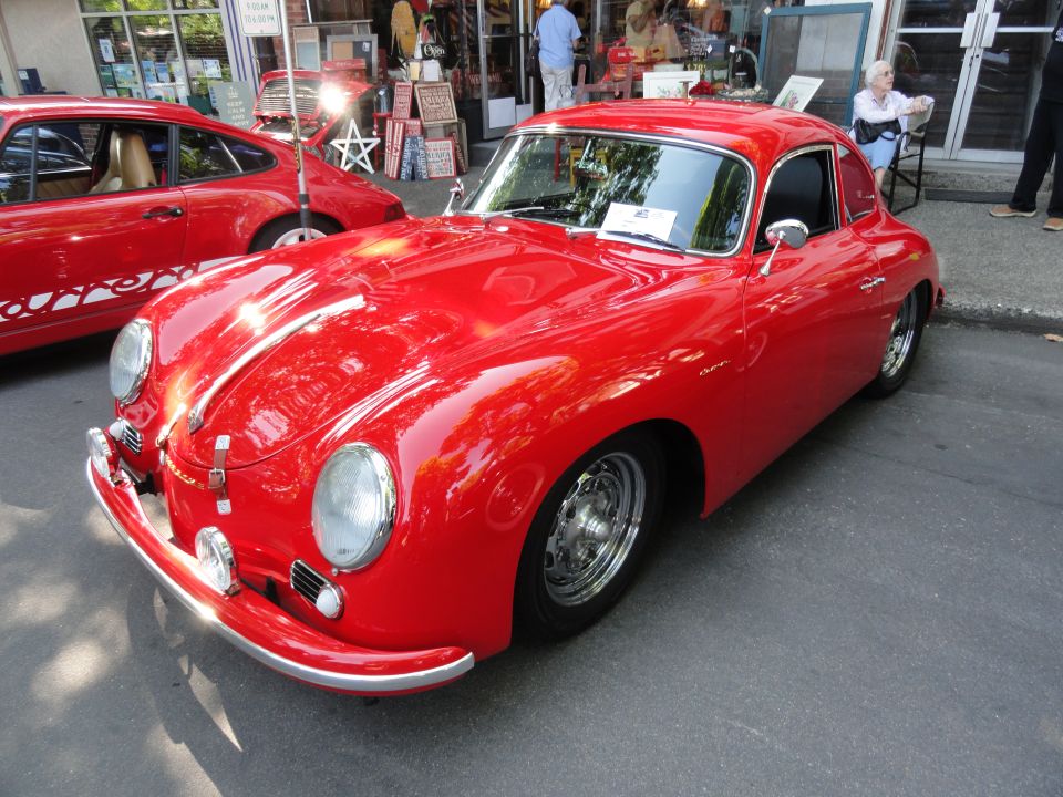 Red coupe with chrome bumper and headlights parked on asphalt. Another red car is visible to the left