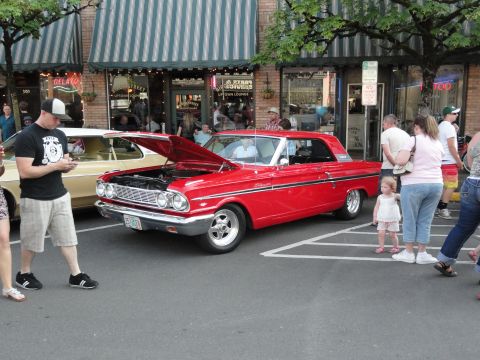 1964 Ford Fairlane - A red 1964 Ford Fairlane coupe is displayed with its hood open, alongside another car and onlookers.