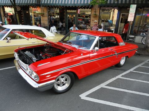 1964 Ford Fairlane - A bright red 1964 Ford Fairlane is displayed with its hood open, parked next to another vehicle on a street.