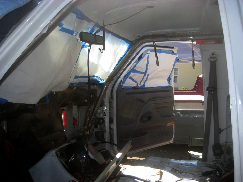 Interior of a vehicle with windows taped off and a roll cage installed. The door is open, showing the dashboard and seats