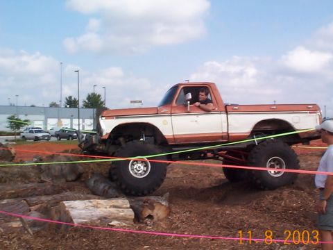 1992 Ford Bronco - A lifted pickup truck navigates an off-road course with logs and dirt obstacles.