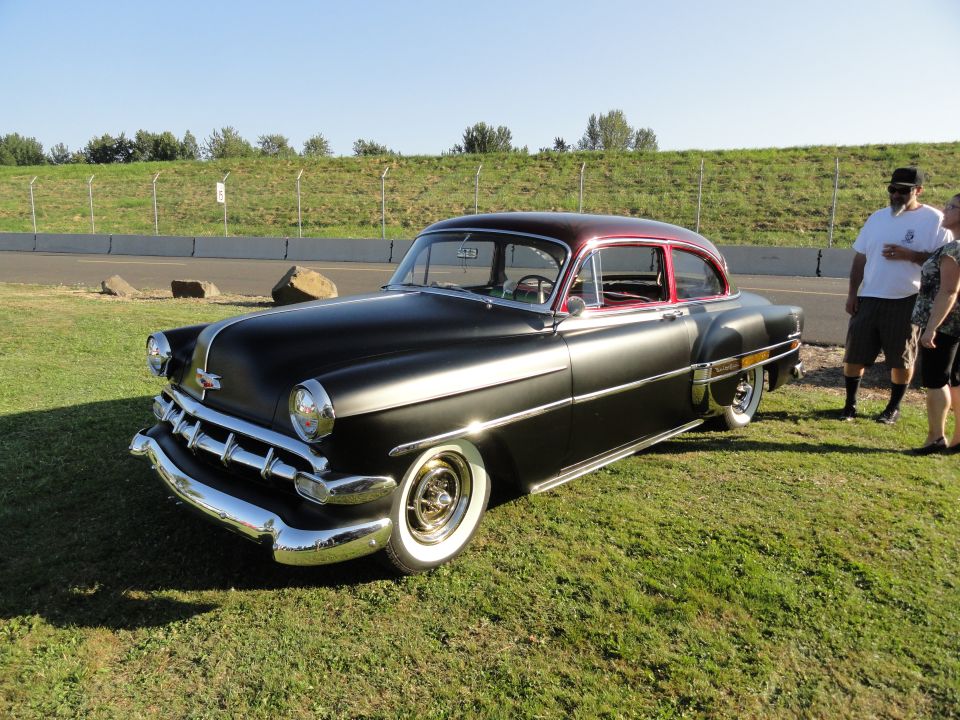 Black and maroon 1953 Chevrolet sedan parked on grass with two people standing nearby