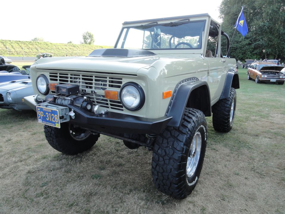 Tan Ford Bronco with large tires, winch, and aftermarket bumper. Oregon license plate 9P-3128 visible. Another car is parked behind it