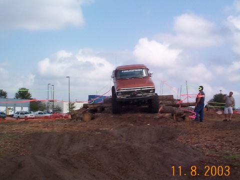 1992 Ford Bronco - A red truck navigates an obstacle course made of logs on a dirt track.