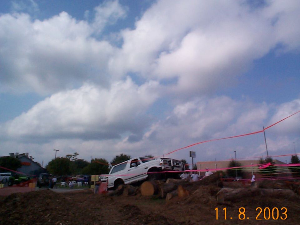 White Ford Bronco climbing a log obstacle at a roped-off 4x4 event, dated 11-8-2003