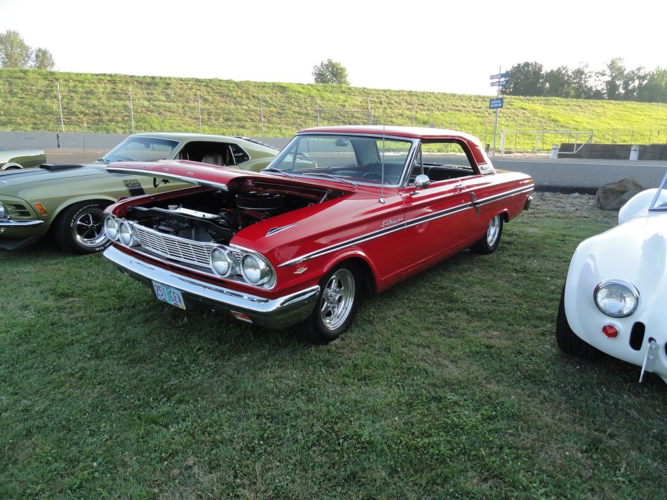 1964 Ford Fairlane with hood open, parked on grass next to a green Mustang and a white sports car