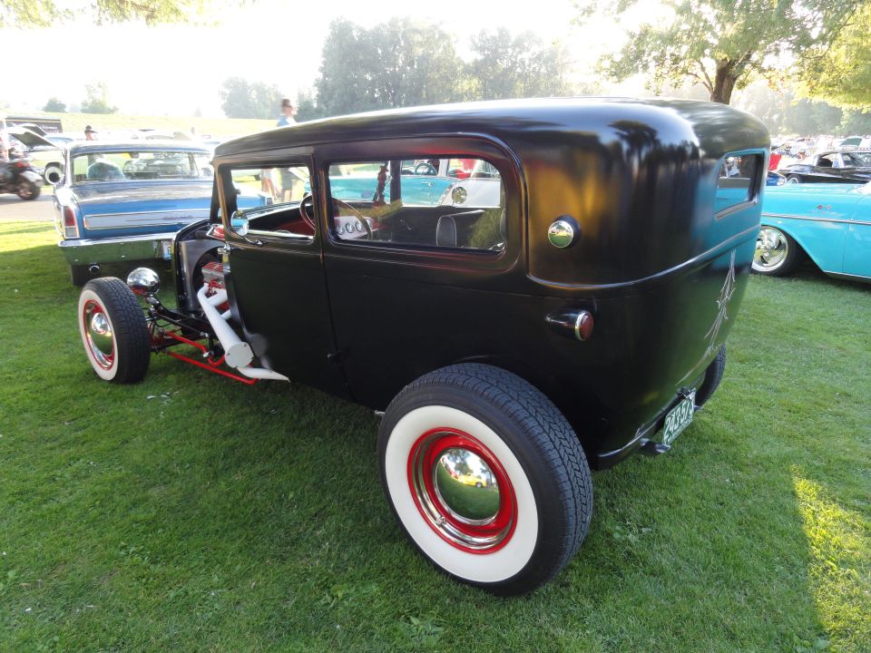 Black hot rod sedan with red wheels and white wall tires, parked on grass