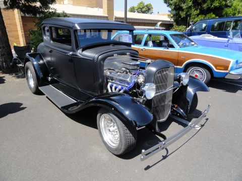 1964 Ford Fairlane - A black hot rod coupe is parked next to a blue woodie wagon and a blue van.