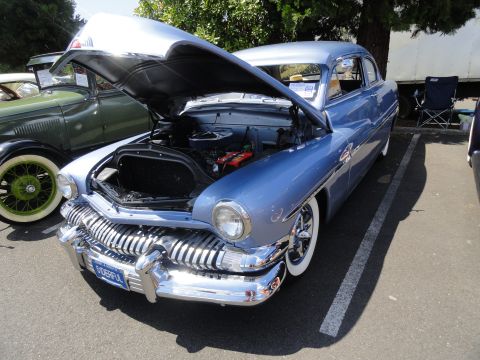 1964 Ford Fairlane - A blue sedan from the 1950s is displayed with its hood open, parked beside another classic vehicle.