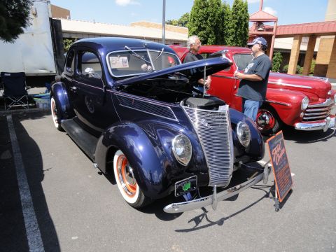 1964 Ford Fairlane - A dark blue 1939 Ford coupe is displayed with its hood open, parked next to a red vehicle. A sign in front of the coupe reads "Ford Coupe".
