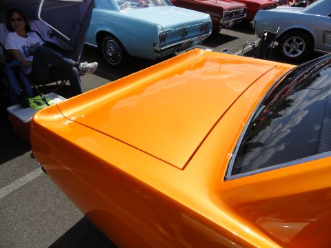 1964 Ford Fairlane - Close-up of an orange 1967 Ford Mustang fastback's trunk, with other classic cars in the background.