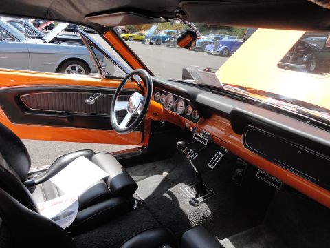 1964 Ford Fairlane - The interior of an orange 1965 Ford Mustang convertible, aftermarket gauges and a manual transmission. Other classic cars are visible in th…