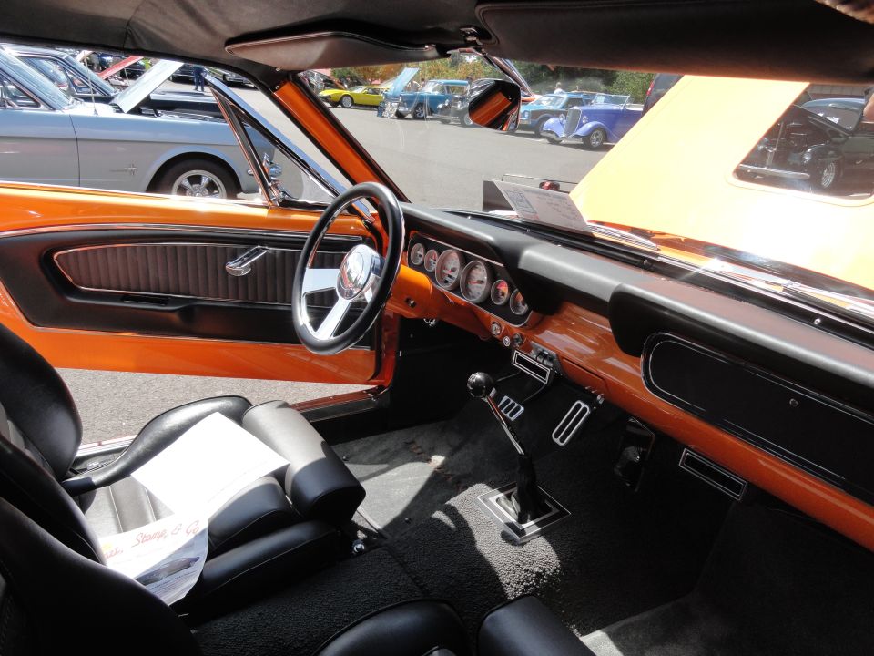 Orange interior with aftermarket gauges and black seats. A 1965 Mustang is visible outside