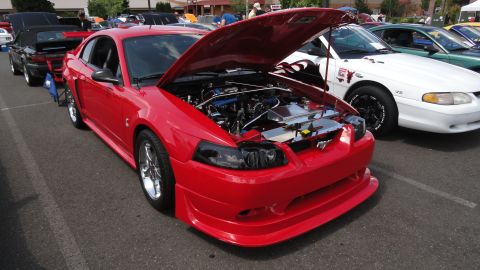 1964 Ford Fairlane - A red 1999 Ford Mustang is parked with its hood open, revealing the engine, alongside other vehicles.