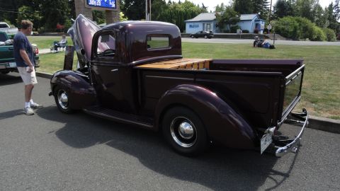 1964 Ford Fairlane - A classic maroon pickup truck with a wooden bed is displayed with its hood up, parked on an asphalt surface.