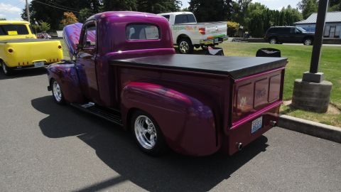 1964 Ford Fairlane - A custom purple pickup truck is parked next to a yellow truck, with other vehicles in the background.