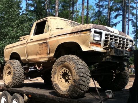1979 Ford F-150 - Mud-splattered 1979 Ford F-150 pickup truck with custom lift and oversized tires loaded onto a trailer.