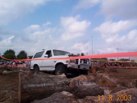 1992 Ford Bronco - A white 1992 Ford Bronco tackles an obstacle course marked by a red ribbon, with logs and dirt surrounding it.