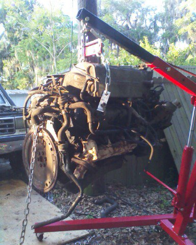 1988 Ford Bronco - Engine removed from a vehicle and suspended by a red engine hoist.