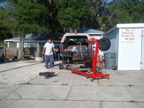 1988 Ford Bronco - An engine is being removed from a vehicle with an engine hoist in a driveway.